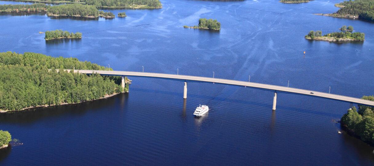 Lake Saimaa and forests are in the picture. Middle of the lake a boat is going under the bridge.