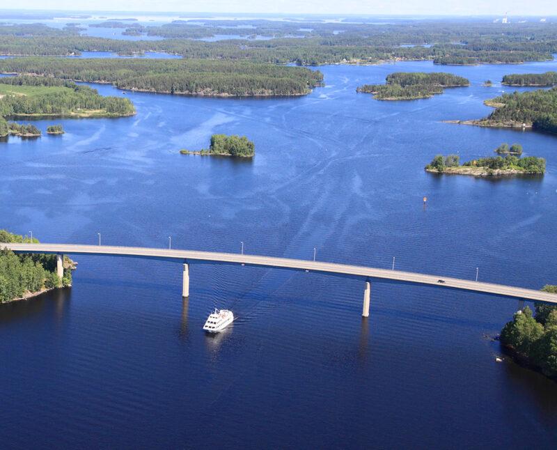 Lake Saimaa and nature from above. In the middle of the picture is a bridge and a boat is going under it.